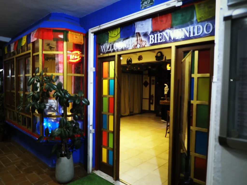 Entrada del restaurante The Everest en Dénia, con vidrieras de colores y banderas de oración